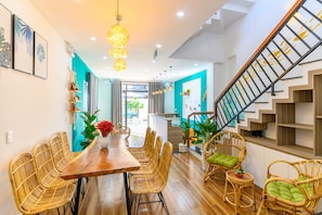 A modern interior with a wooden dining table, wicker chairs, and a staircase with a glass railing. - Kivi Homestay (Da Nang)