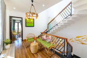 A modern living room with a staircase, wicker furniture, and a green sofa. - Kivi Homestay (Da Nang)