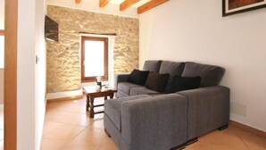 Un salon avec un canapé gris, une petite table en bois, un mur en pierre et une poutre en bois au plafond.
