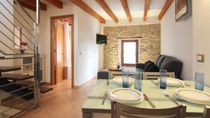 Un coin repas avec une table dressée pour quatre personnes, un canapé, un mur en pierre et un escalier.