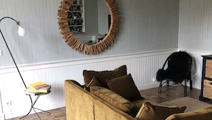 A living room with a sofa, a round mirror, a floor lamp, and a patterned rug. - Villa Saint-Armand - Chambres d'hotes (Salles)