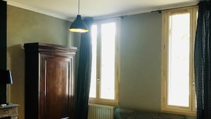 A bedroom with a bed, a wooden wardrobe, a radiator, a bench, and a window with curtains. - Villa Saint-Armand - Chambres d'hotes (Salles)