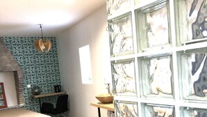 A bedroom with a patterned wallpaper, a bed with a striped blanket, a hanging light fixture, and a tiled floor. - Villa Saint-Armand - Chambres d'hotes (Salles)