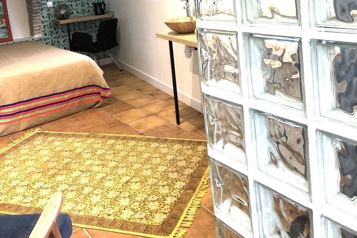 Een slaapkamer met behang met een patroon, een bed met een gestreept deken, een hanglamp en een betegelde vloer.