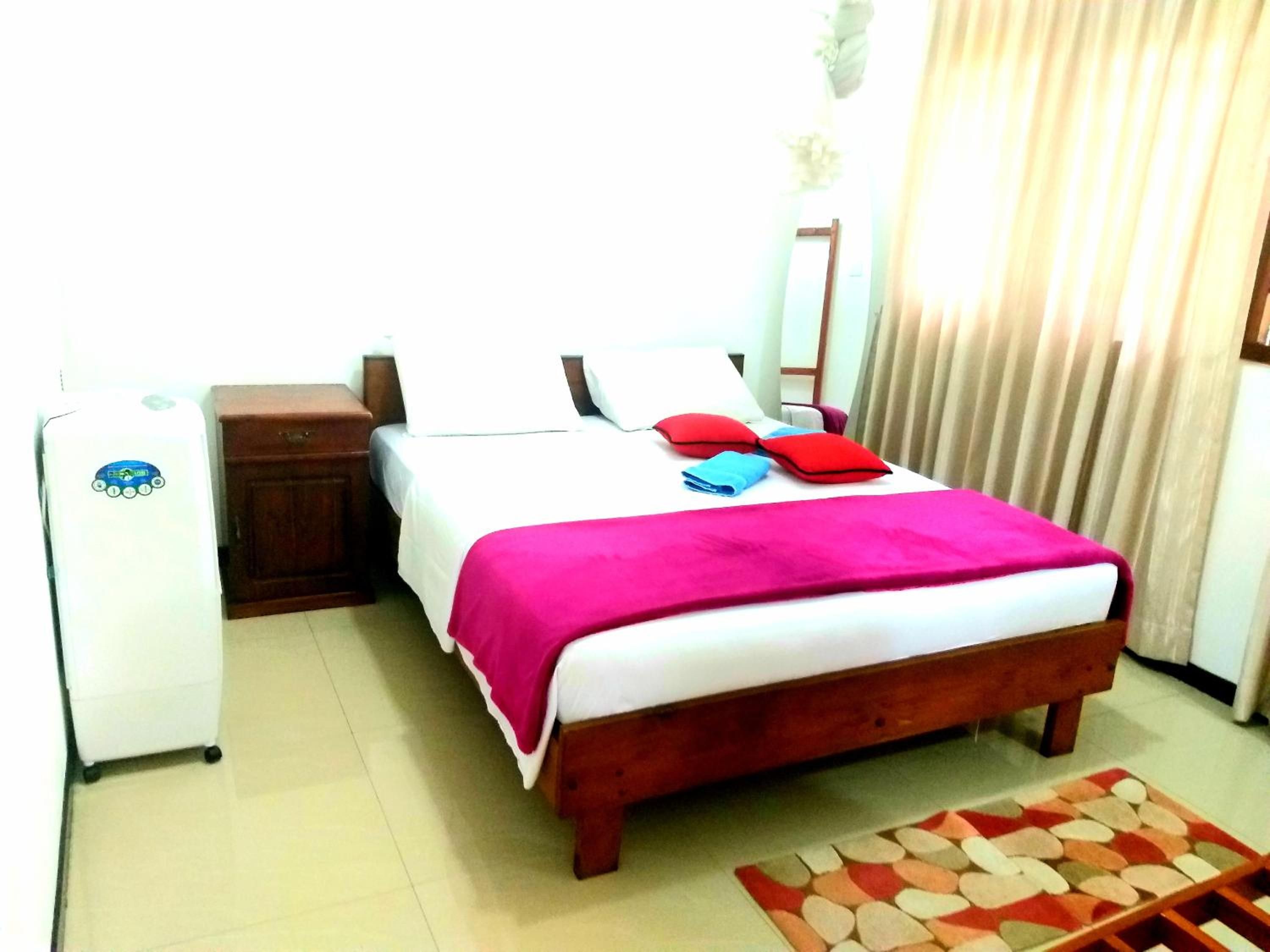 A hotel room with a bed, a nightstand, a white appliance, and a window with curtains.