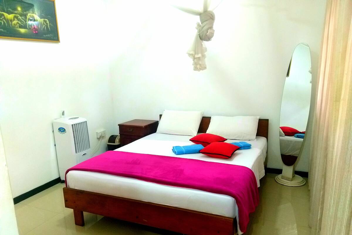 A hotel room with a bed, bedside table, mirror, and a heater.