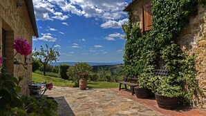 A stone patio with a bench, potted plants, and a view of a rural landscape. - La Scaletta Della Rocca (Castellina in Chianti)