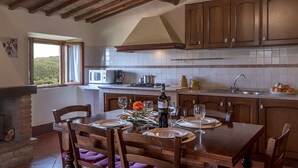 A kitchen with wooden cabinets, a stone fireplace, and a dining table set for a meal. - La Scaletta Della Rocca (Castellina in Chianti)