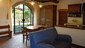 A rustic interior with a dining table, chairs, a blue sofa, wooden cabinets, and a large arched window. - Romantic With Chianti Panorama (Bucine)