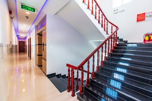 A hotel corridor with a polished floor, a red wooden staircase, and a fire extinguisher on the wall.