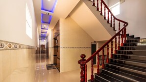 A modern hotel lobby with a polished marble floor, a wooden staircase with red balusters, and a geometric patterned border along the walls.