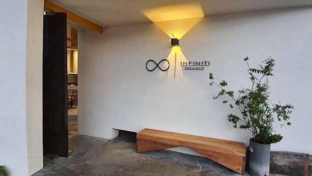 A modern entrance with a wooden bench, a potted plant, and a wall-mounted sign for 'INFINITI CAFE & RESTO'.