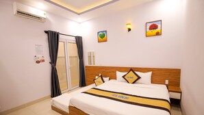 A hotel room with a bed, a window with curtains, an air conditioner, a wall-mounted light, and a painting.