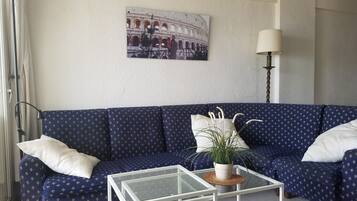 A living room with a blue sofa, a glass coffee table, a lamp, and a picture of the Colosseum on the wall.