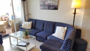 A living room with a blue patterned sofa, a glass coffee table, a lamp, and a picture of the Colosseum on the wall. - Apartamento Las Torres Con Vista Al Mar (Fuengirola)