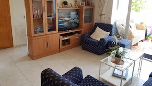 A living room with a TV, wooden cabinet, blue patterned sofa, and a small table with a plant. - Apartamento Las Torres Con Vista Al Mar (Fuengirola)