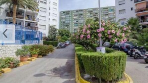 A residential area with high-rise buildings, a street with parked cars, and a well-maintained garden with a spherical street lamp. - Apartamento Las Torres Con Vista Al Mar (Fuengirola)
