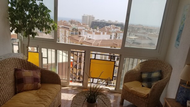 A spacious balcony with wicker furniture, a potted plant, and a view of the cityscape. - Apartamento Las Torres Con Vista Al Mar (Fuengirola)