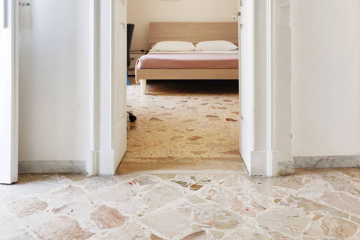 A bedroom with a bed, a painting on the wall, and a patterned floor.
