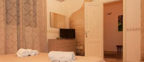 Une chambre d’hôtel avec un lit, un téléviseur posé sur une commode en bois, une porte donnant sur une autre pièce et des rideaux à motifs.