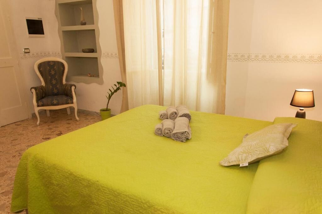 A hotel room with a green bedspread, a chair, a plant, and a lamp.