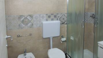 Ein Badezimmer mit Toilette, Bidet und Duschkabine aus Glas.