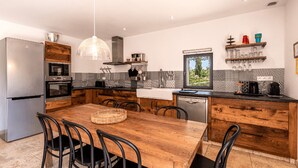 A modern kitchen with a wooden dining table, black chairs, and a large window. - Charming apartments in Porto-Vecchio and Araggio, between the sea and the mounta (PORTO VECCHIO)