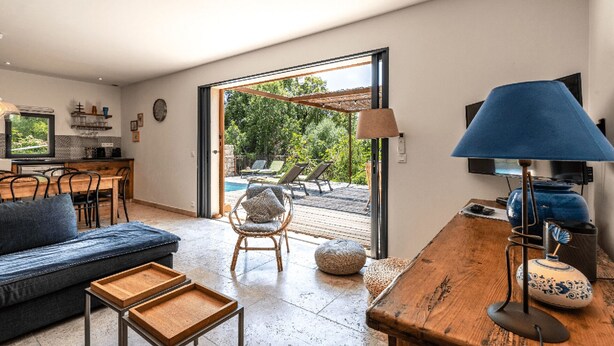A modern living room with a sofa, coffee table, and a dining area. There is a large window with a view of a pool and greenery. - Charming apartments in Porto-Vecchio and Araggio, between the sea and the mounta (PORTO VECCHIO)