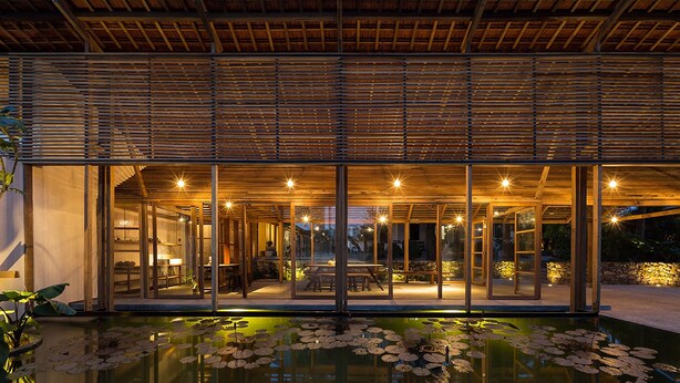 Uma casa moderna com fachada de vidro, deck de madeira e um lago com nenúfares.