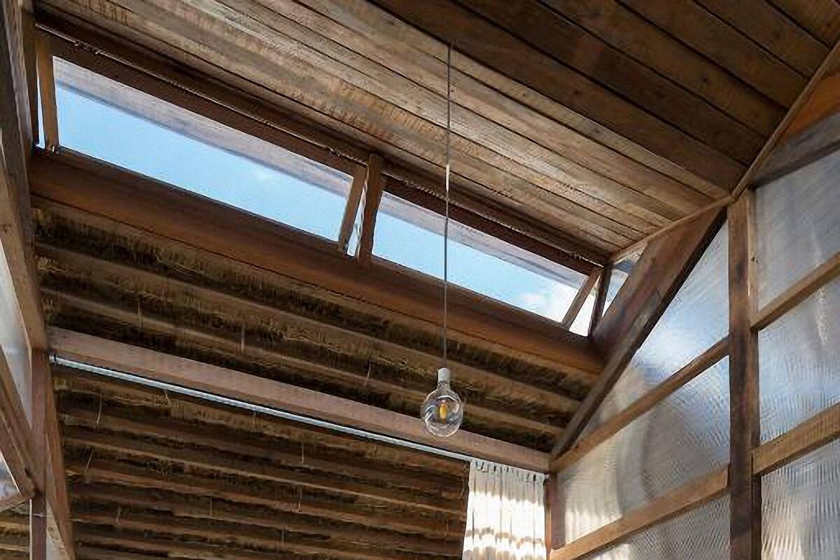 Una cabaña rústica con techo de madera, literas, una silla y ventanas amplias.