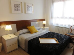 Ein Hotelzimmer mit einem Bett, zwei Nachttischen, einem Sessel, einer Heizung und zwei gerahmten Bildern an der Wand.