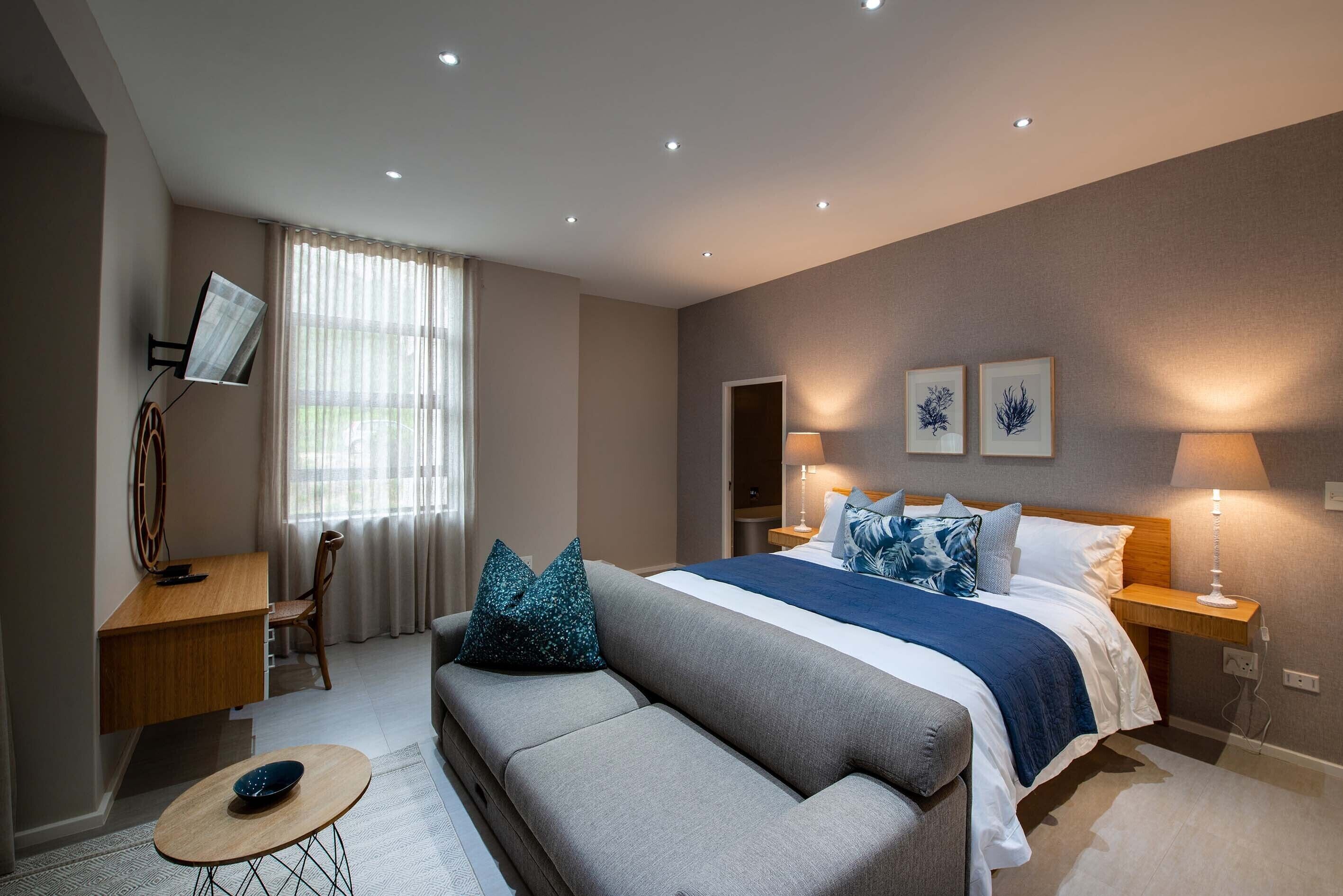 Quarto de hotel moderno com uma cama grande, um sofá, uma escrivaninha e uma janela com cortinas.