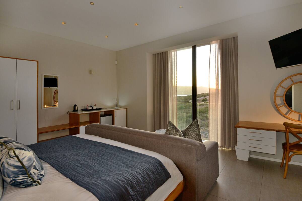 A hotel room with a bed, a desk, a chair, a TV, and a view of the outdoors.