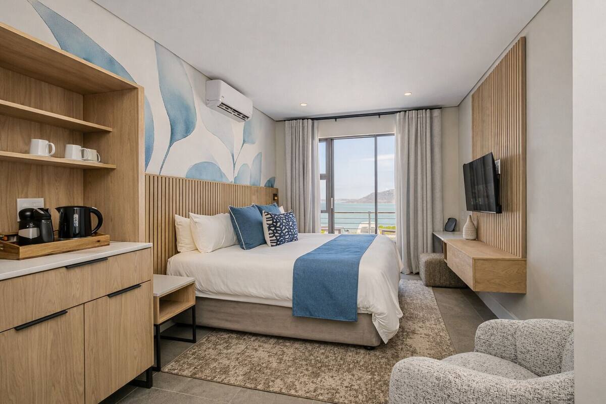 A modern hotel room with a bed, a TV, a coffee machine, and a view of the sea.