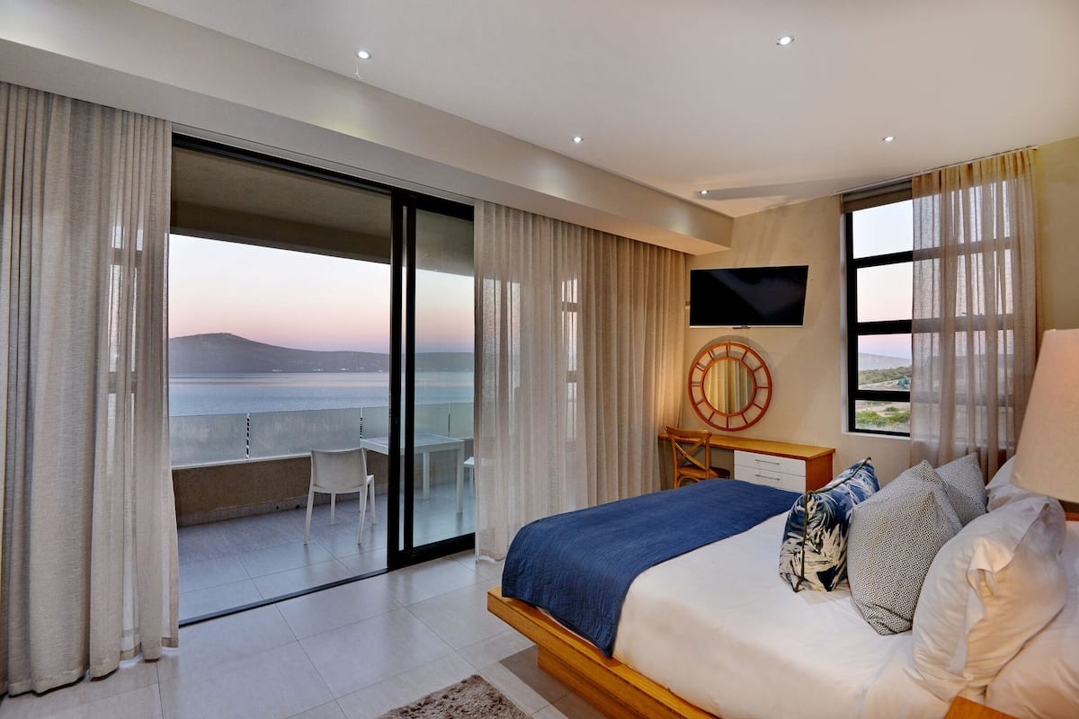 A bedroom with a bed, a TV, a desk, and a view of the sea.