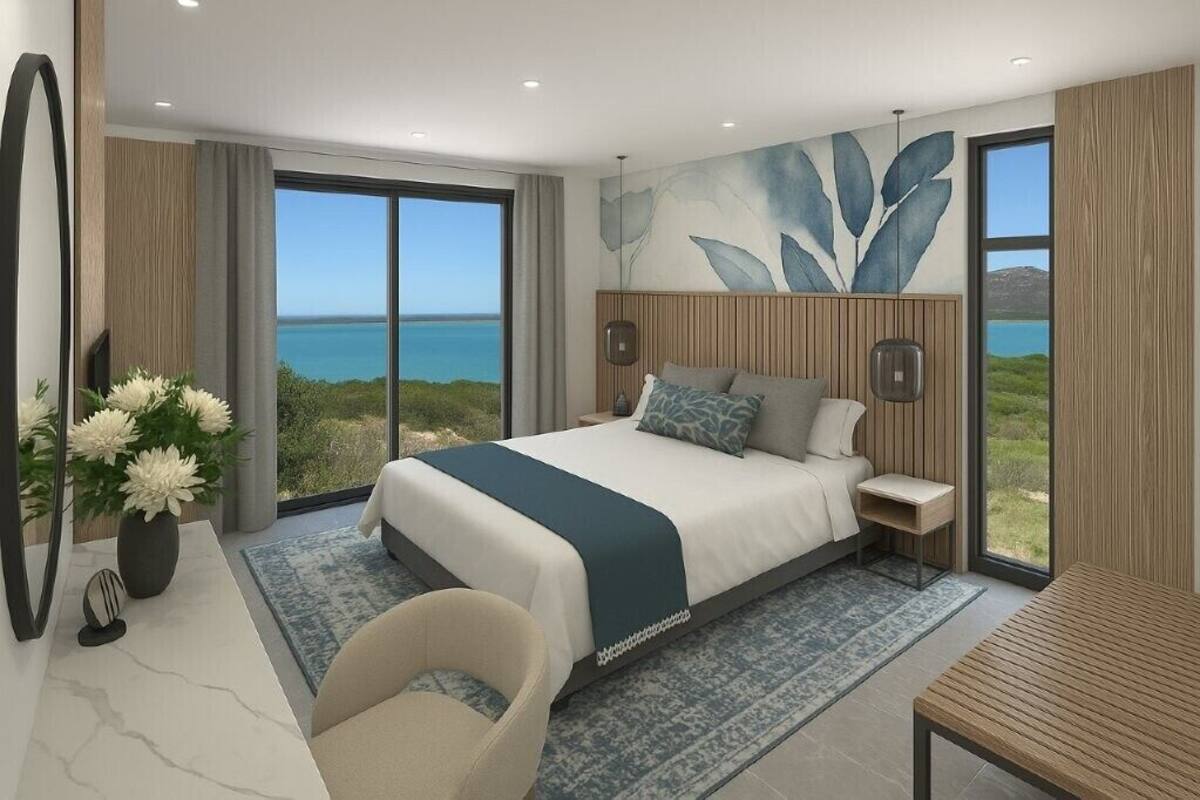 A modern bedroom with a large bed, a view of the sea, and a wooden headboard.