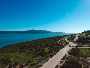 Carretera costera que lleva a un acantilado con vista al mar y montañas distantes.