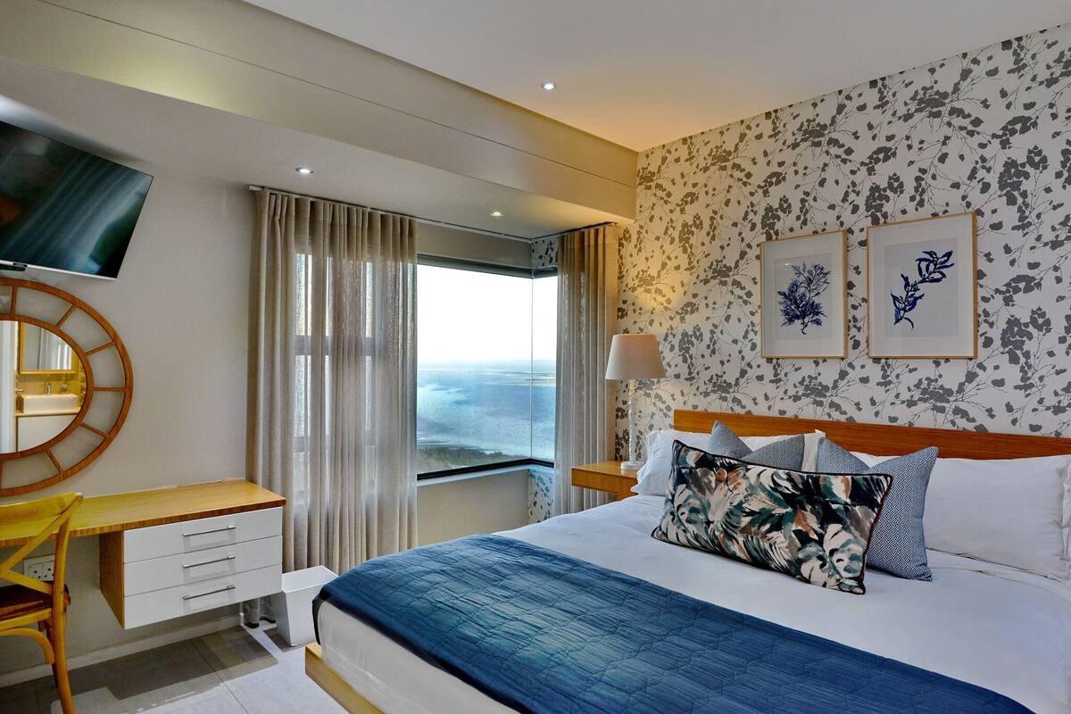 A hotel room with a bed, a desk, a chair, a TV, and a window with curtains.