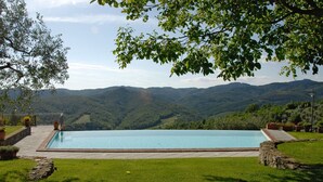 Une piscine rectangulaire bordée de pierres, entourée d’une pelouse bien entretenue et de plantes en pot, le tout se dressant sur un fond de collines douces et sous un ciel dégagé.