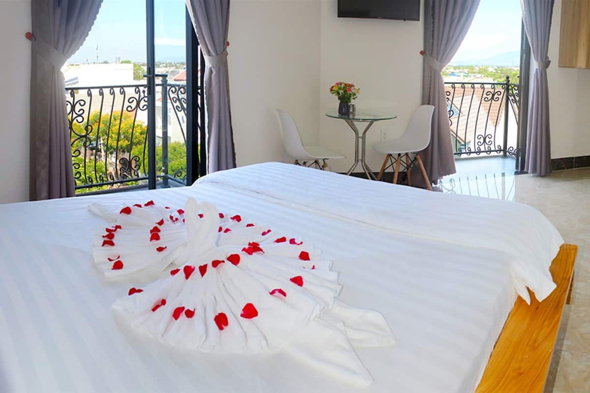 Habitación de hotel con una cama grande, una mesita con una silla y un balcón con vistas.