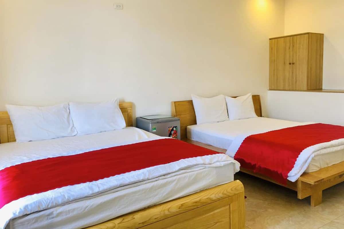 Habitación de hotel con dos camas, cada una con ropa blanca y mantas rojas, un cabecero de madera, una mesita de noche con lámpara y un armario de madera.