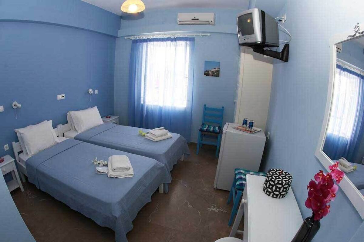 Quarto com duas camas, uma escrivaninha, uma cadeira, uma televisão e um espelho.