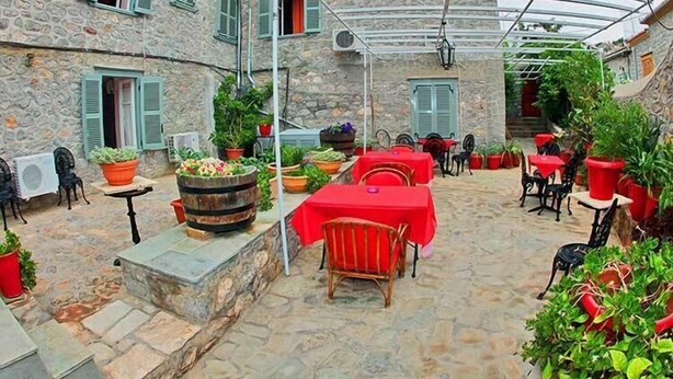 Un edificio de piedra con un patio cubierto que cuenta con mesas, sillas, plantas en macetas y un barril.
