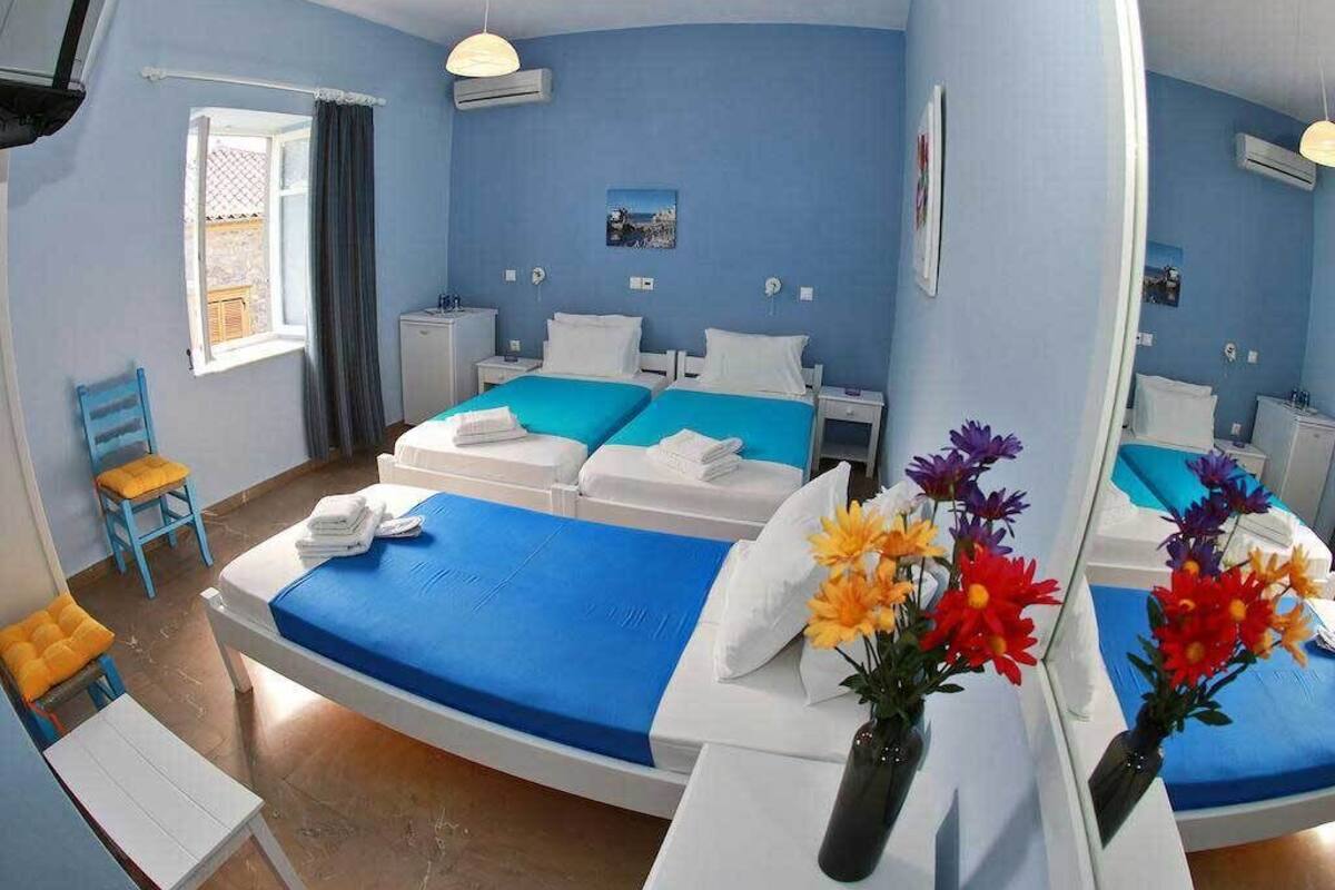 Quarto de hotel com cama arredondada, uma mesa pequena, uma cadeira, janela com cortinas e um espelho.