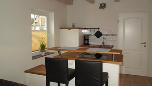 A compact kitchen with a wooden countertop, two black chairs, a window with blinds, and a door. - Apartments with a large balcony near the beach (Bosau)