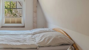 A single bed with a wooden headboard, a bedside table with a lamp, and a window with blinds. - Apartments with a large balcony near the beach (Bosau)