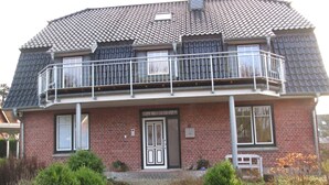 A two-story house with a balcony, a front door, and a chimney. - Apartments with a large balcony near the beach (Bosau)