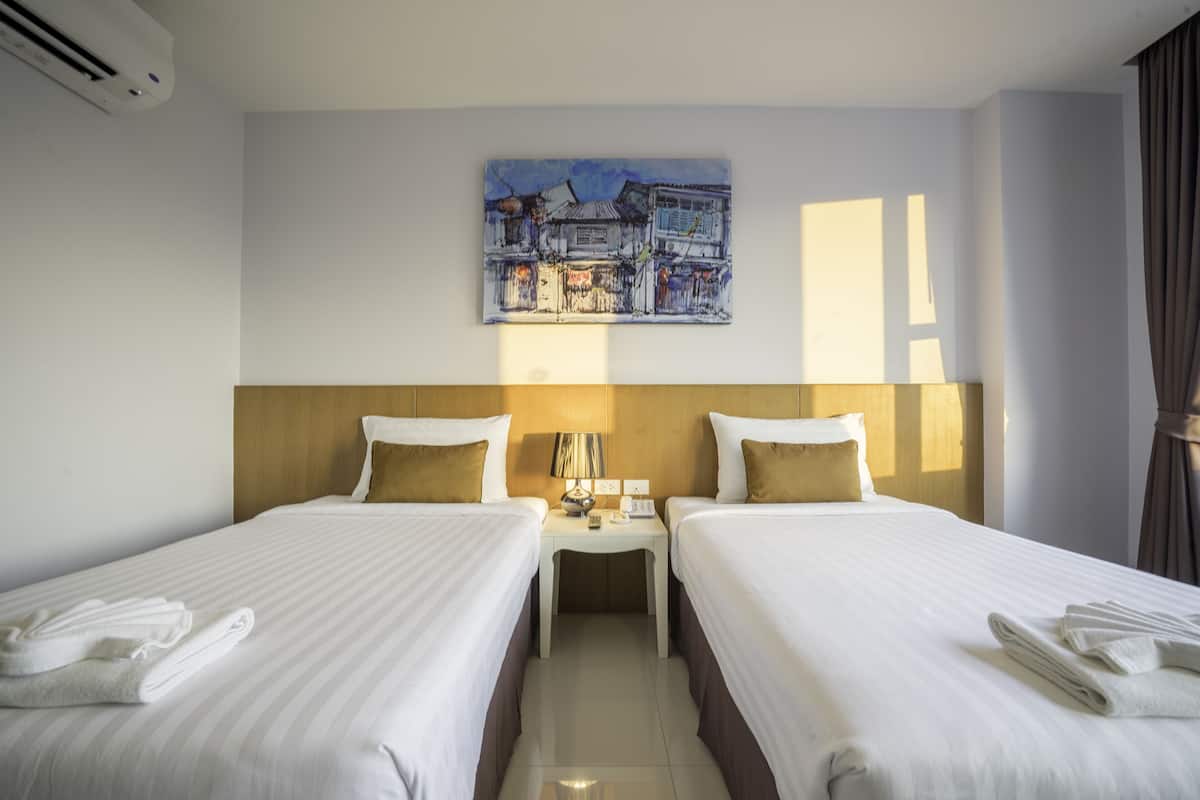 A hotel room with two beds, a nightstand, a lamp, and a painting on the wall.