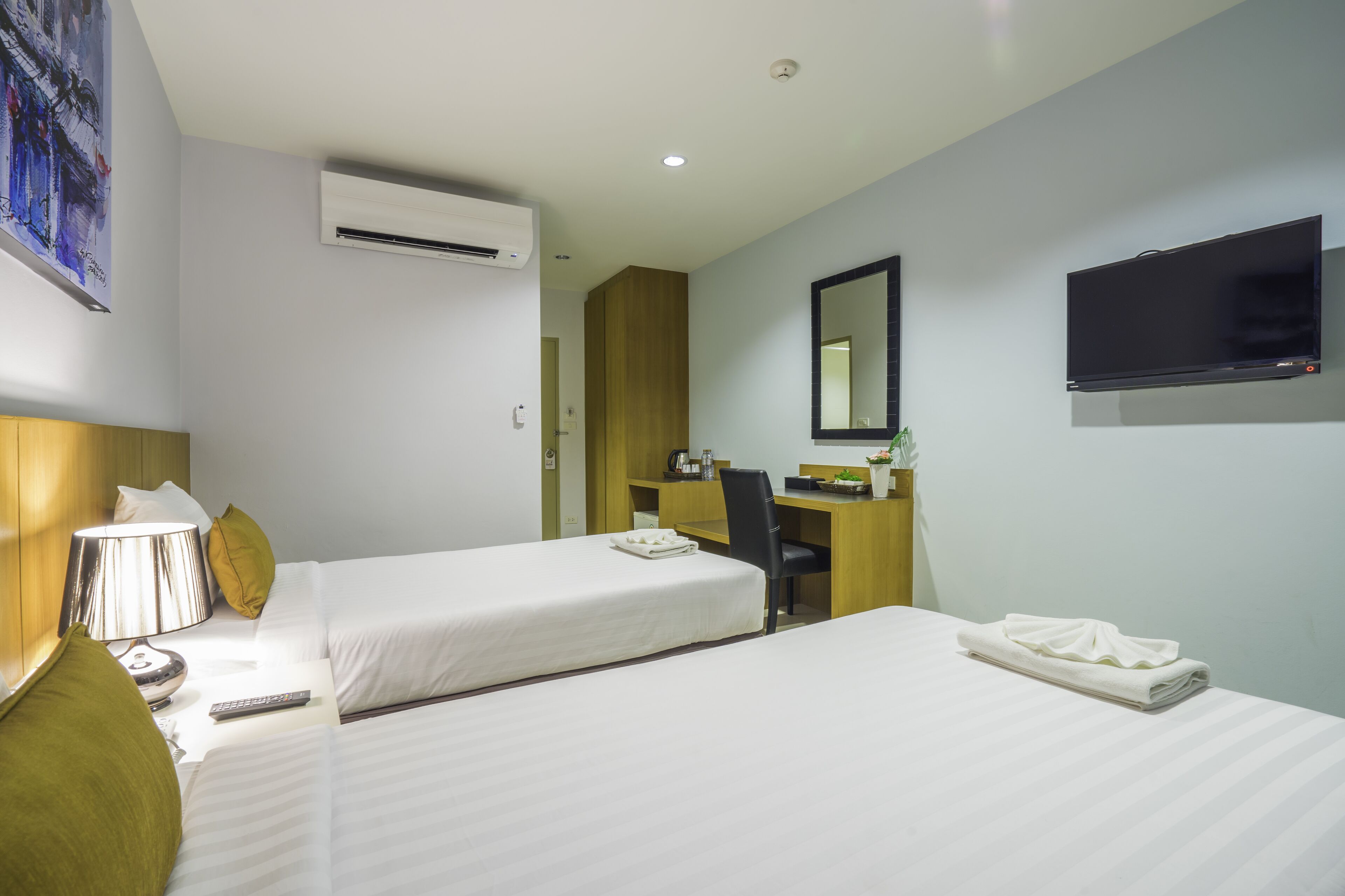 A hotel room with two beds, a desk, a chair, a TV, and an air conditioning unit.