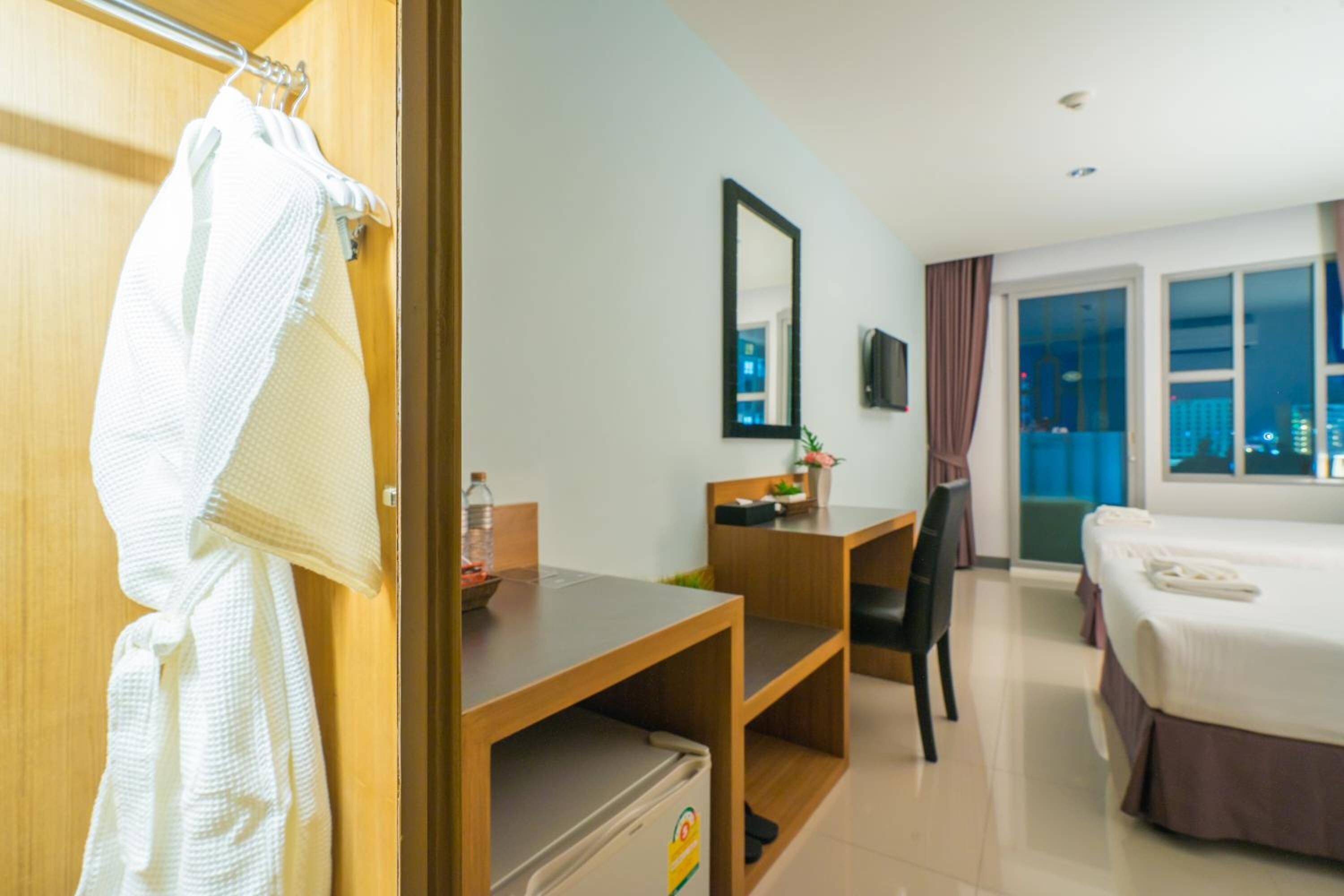 Habitación de hotel con cama, escritorio, silla, armario y ventana con vistas a la ciudad.